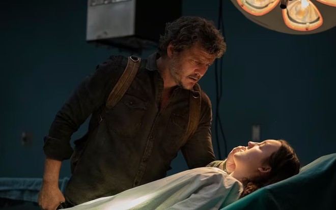Pedro Pascal tem expressão séria enquanto observa Bella Ramsey, que está deitada em uma cama de hospital
