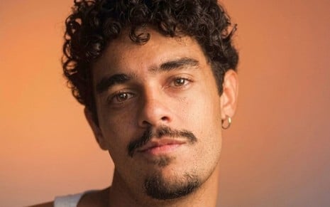 Homem pardo, de cabelos escuros e encaracolados, usando cavanhaque e regata branca.