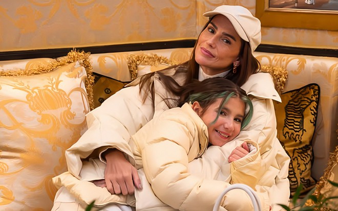 Deborah Secco abraça a filha, Maria Flor, no sofá de um hotel