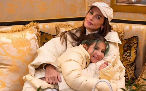 Deborah Secco abraça a filha, Maria Flor, no sofá de um hotel