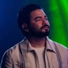 Yudi Tamashiro tem expressão séria em um estúdio, com uma câmera ao seu lado esquerdo e luzes no lado direto