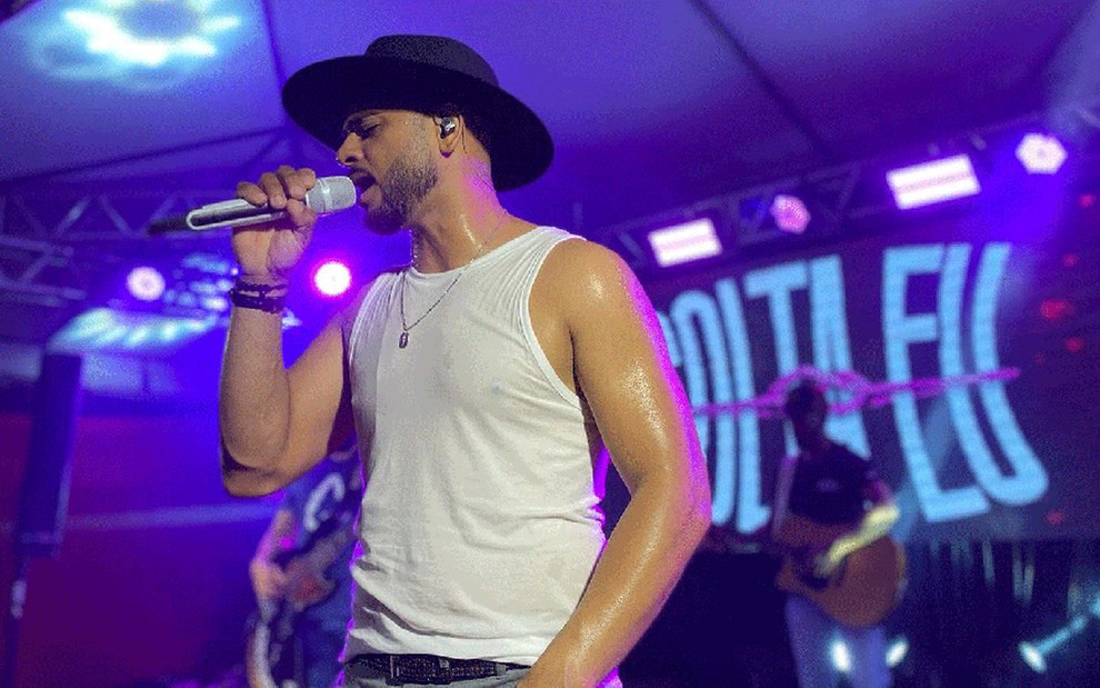 Homem de regata branca e chapéu de caubói canta em show