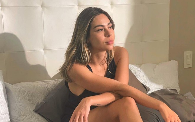 Raira Machado está sentada na cama, com expressão entediada