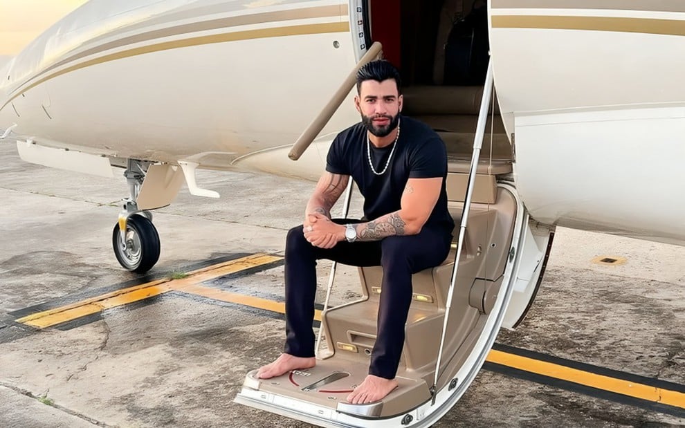 Gusttavo Lima está sentado descalço na escada da entrada de uma aeronave