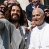 Amor barbudo e de cabelos compridos tira selfie com o papa, que veste trajes brancos e sorri discretamente