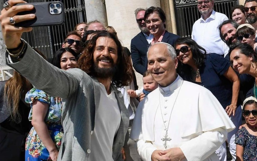 Amor barbudo e de cabelos compridos tira selfie com o papa, que veste trajes brancos e sorri discretamente
