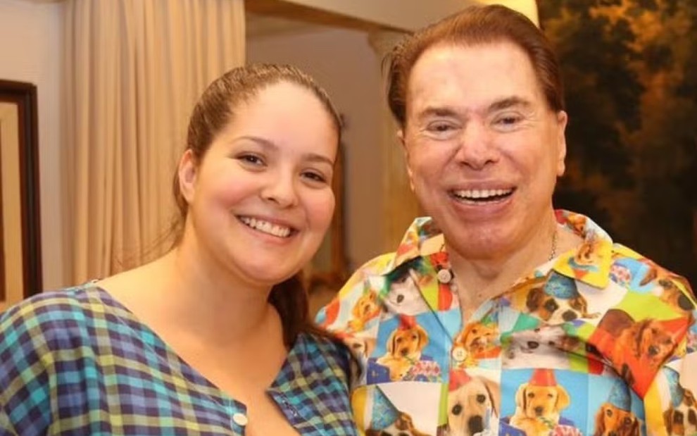 Ligia Abravanel posa sorridente ao lado de Silvio Santos, que usa um pijama colorido