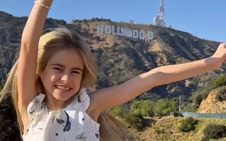 Mel Summers posa diante do letreiro de Hollywood, com os braços para cima e sorriso aberto