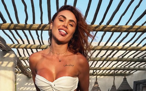 Natacha Horana posa com a língua de fora; ela usa um top branco sem alças