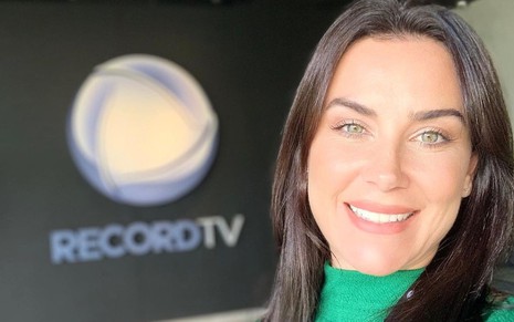 Larissa Erthal posa sorridente diante de logo da Record