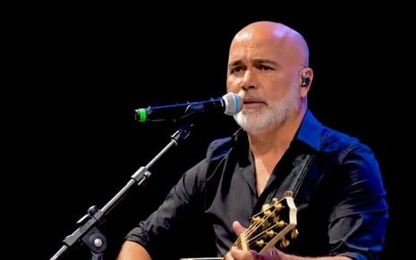 Rick Sollo toca violão e canta em microfone durante show