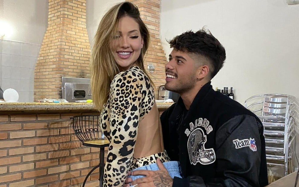 Virginia Fonseca está sentada no colo de Zé Felipe, os dois sorridentes, em uma área de churrasqueira