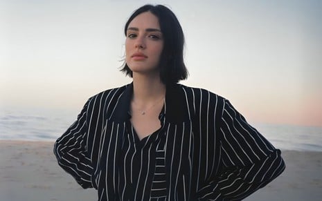 Isabelle Drummond posando em frente ao mar, em Ipanema no Rio de Janeiro, com roupa listrada e mãos na cintura