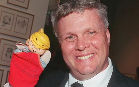 Jay North sorri e segura um boneco do personagem Dennis, o Pimentinha