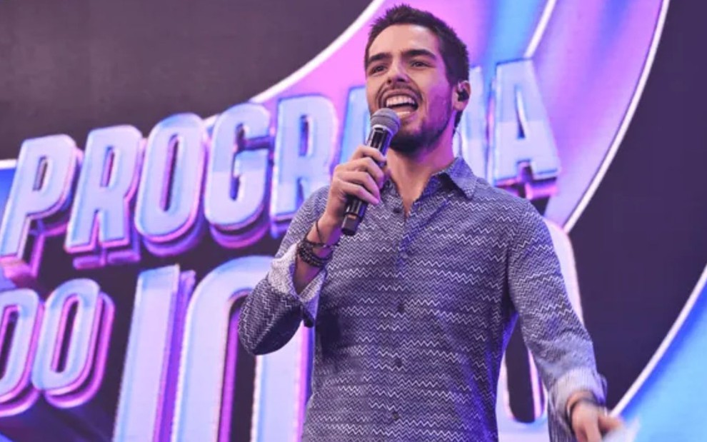 João Silva no Programa do João, na Band; ele segura microfone em frente ao logo e aparece sorridente