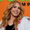 Joelma sorridente, posando com um casaco branco, em frente a uma parede laranja