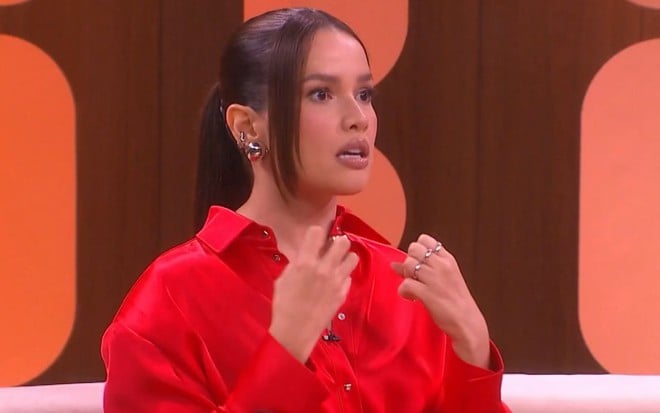 Juliette Freire em sua estreia no Saia Justa; ela está sentada no sofá, de camisa vermelha, com expressão de medo