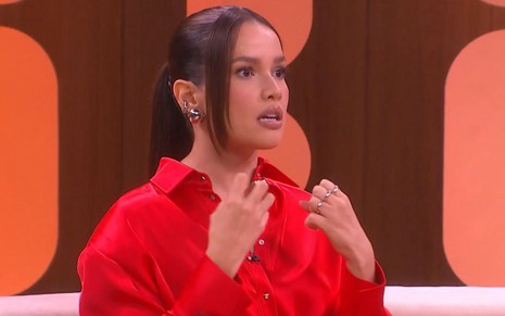 Juliette Freire em sua estreia no Saia Justa; ela está sentada no sofá, de camisa vermelha, com expressão de medo