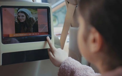 Nisan (Kübra Süzgün) olha para TV no carro em cena da novela Força de Mulher