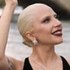 Lady Gaga acena com a mão direita e sorri discretamente