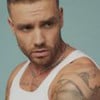 Liam Payne está com o corpo de lado, veste uma regata branca, e olha para a esquerda