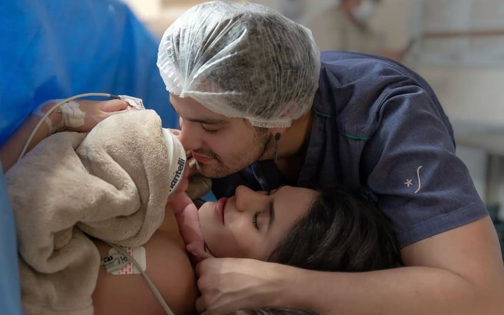 Luan Santana abraça Jade Magalhães, que está com Serena nos braços; o rosto da menina está coberto por uma touca