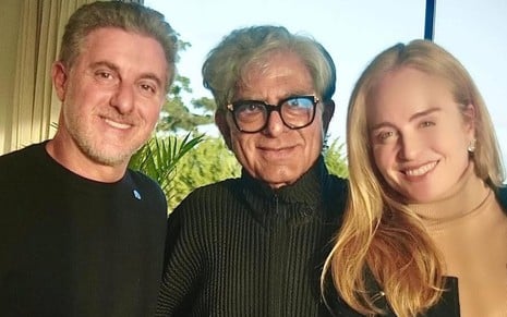 Luciano Huck, Deepak Chopra e Angélica sorridentes lado a lado, usando roupas pretas