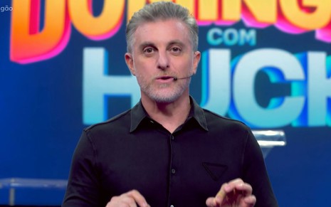 O apresentador Luciano Huck à frente de um telão em que se lê Domingão com Huck