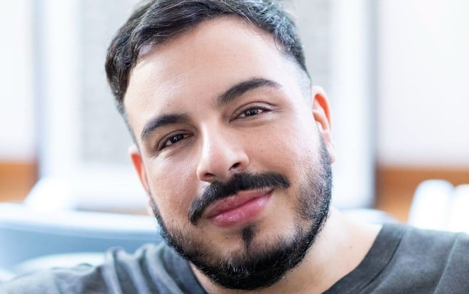 Luis Lobianco sorri discretamente em foto; ele usa camiseta preta, está com cabelos curtos e usa barba