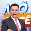 Apresentador gesticula com expressão séria em frente ao letreiro colorido do programa “Alô, Você"