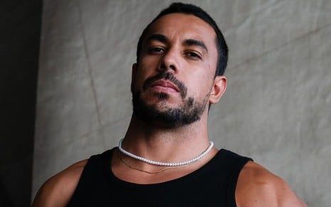 Maike Cruz posando em foto para o Instagram, com feição séria, usando regata preta e colar branco