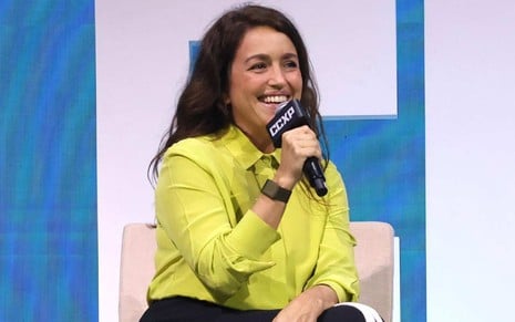 A autora Manuela Dias sorrindo, com microfone em frente ao rosto, em painel de Vale Tudo na CCXP 24