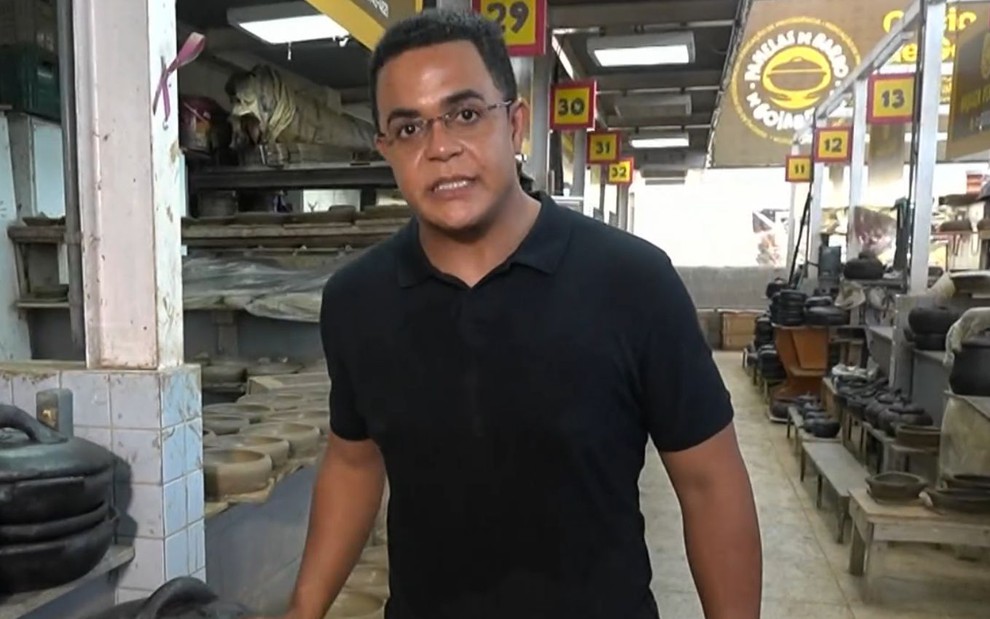 Marcelo Pereira usa uma camiseta preta e está num galpão cheio de panelas de barro