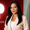Márcia Dantas posando com terno bege em frente ao logo da Jovem Pan