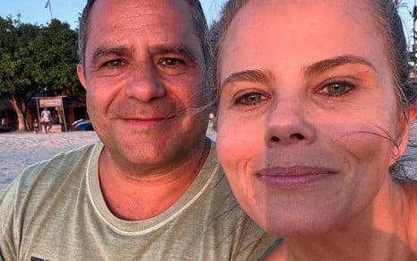 Patrick e Maria Cândida sentados na praia, sorridentes, de frente para a luz do pôr-do-sol