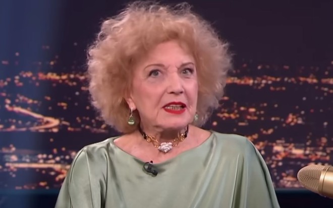 Marisa Paredes no Late Xou da RTVE; atriz usa vestido verde e está sentada em frente a uma tela que imita uma cidade à noite