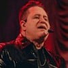 Marrone em cima do palco, com microfone, cantando; fundo é totalmente vermelho
