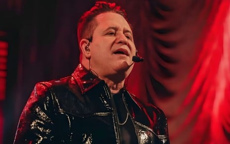Marrone em cima do palco, com microfone, cantando; fundo é totalmente vermelho