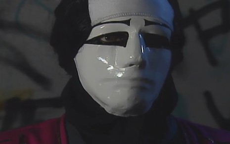 O ator Breno Moroni com máscara branca, caracterizado como o personagem Mascarado na novela A Viagem