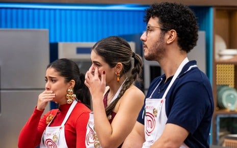 três cozinheiros se alinham, aos prantos, em reality show; eles vestem o avental do masterchef