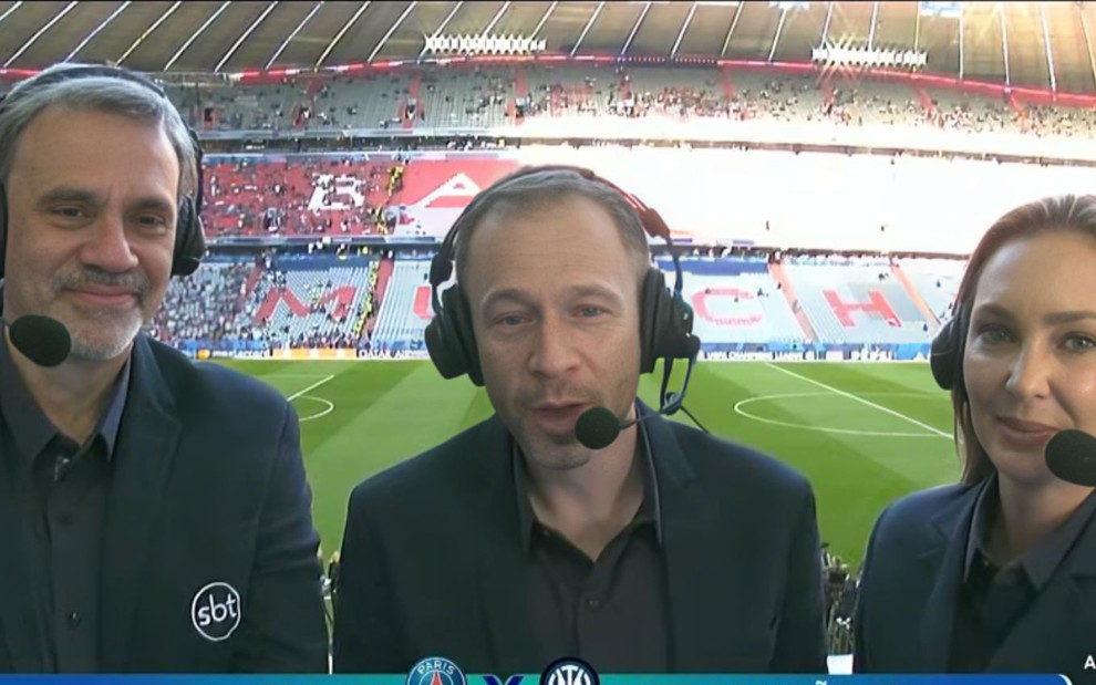 Trio de comentaristas do SBT aparece em cabine de transmissão durante jogo entre PSG e Inter de Milão, com estádio ao fundo.