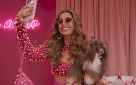 Camila Pitanga usa roupa rosa escandalosa e tira selfie com um cachorro no colo