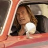 Com cabelos compridos, Josh Holloway está dentro de um carro vermelho e tem uma expressão sacana