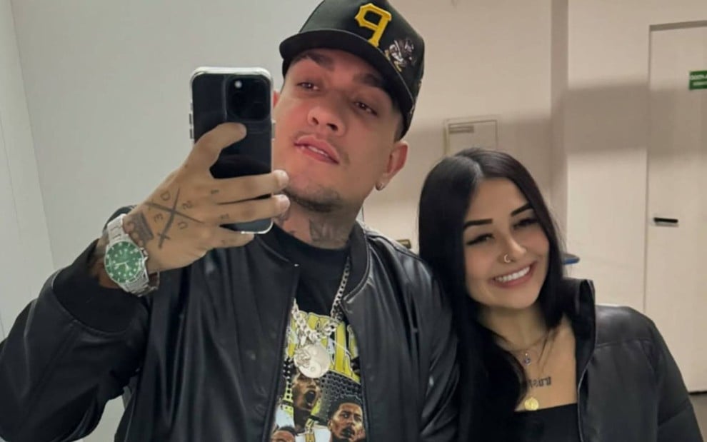 MC Binn e Ana Laura Marques em selfie tirada no espelho; cantor segura celular na mão e usa um boné