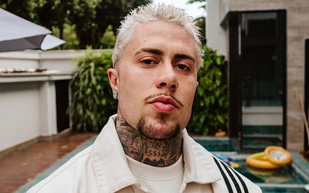 MC Daniel posando em frente a uma piscina, com uma jaqueta off-white, cabelo loiro e cavanhaque castanho