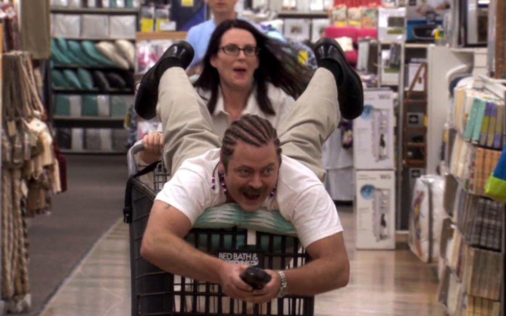 Megan Mullally empurrando um carrinho de supermercado com Nick Offerman em cima em cena de Parks and Recreation
