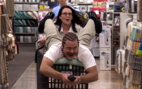 Megan Mullally empurrando um carrinho de supermercado com Nick Offerman em cima em cena de Parks and Recreation
