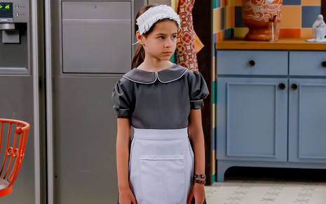 Anna (Mel Summers) com expressão triste e usando uniforme de empregada em cena da novela A Caverna Encantada