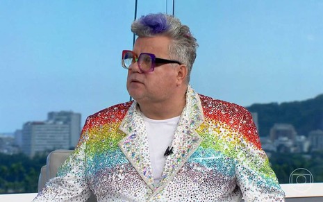 O comentarista de Carnaval Milton Cunha com terno brilhante, com as cores do arco-íris, em transmissão da Globo