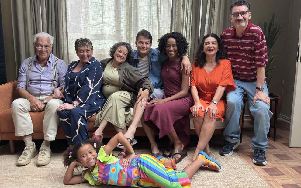 Elenco principal da nova versão da série infantil Mundo da Lua posando para foto, adultos sentados no sofá e menina deitada no chão